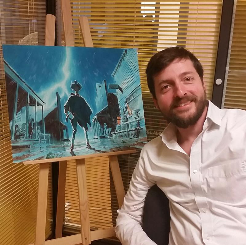 Matthieu Bonhomme devant l'illustration originale de couverture de son album hommage à Lucky Luke